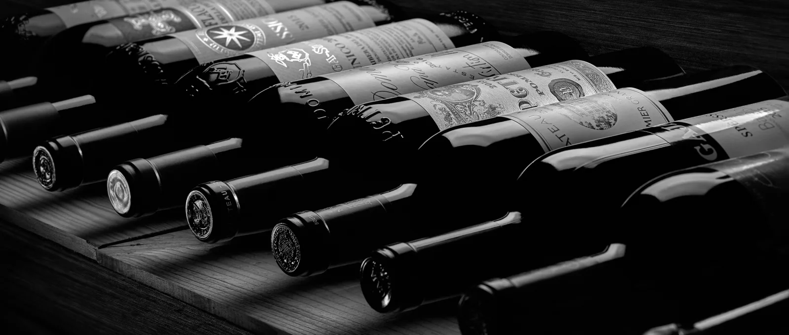 Botellas de vino de alta gama tumbadas sobre un botellero de madera oscura, en un blanco y negro dramático · Fotografía de producto, TimeLäB Studio Barcelona