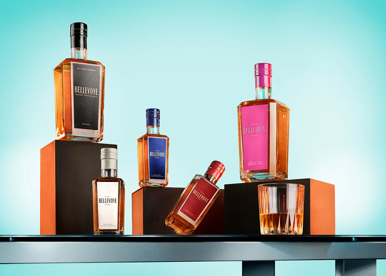 Botellas de whisky Bellevoye dispuestas sobre pedestales, sobre fondo turquesa · Fotografía de producto, TimeLäB Studio Barcelona